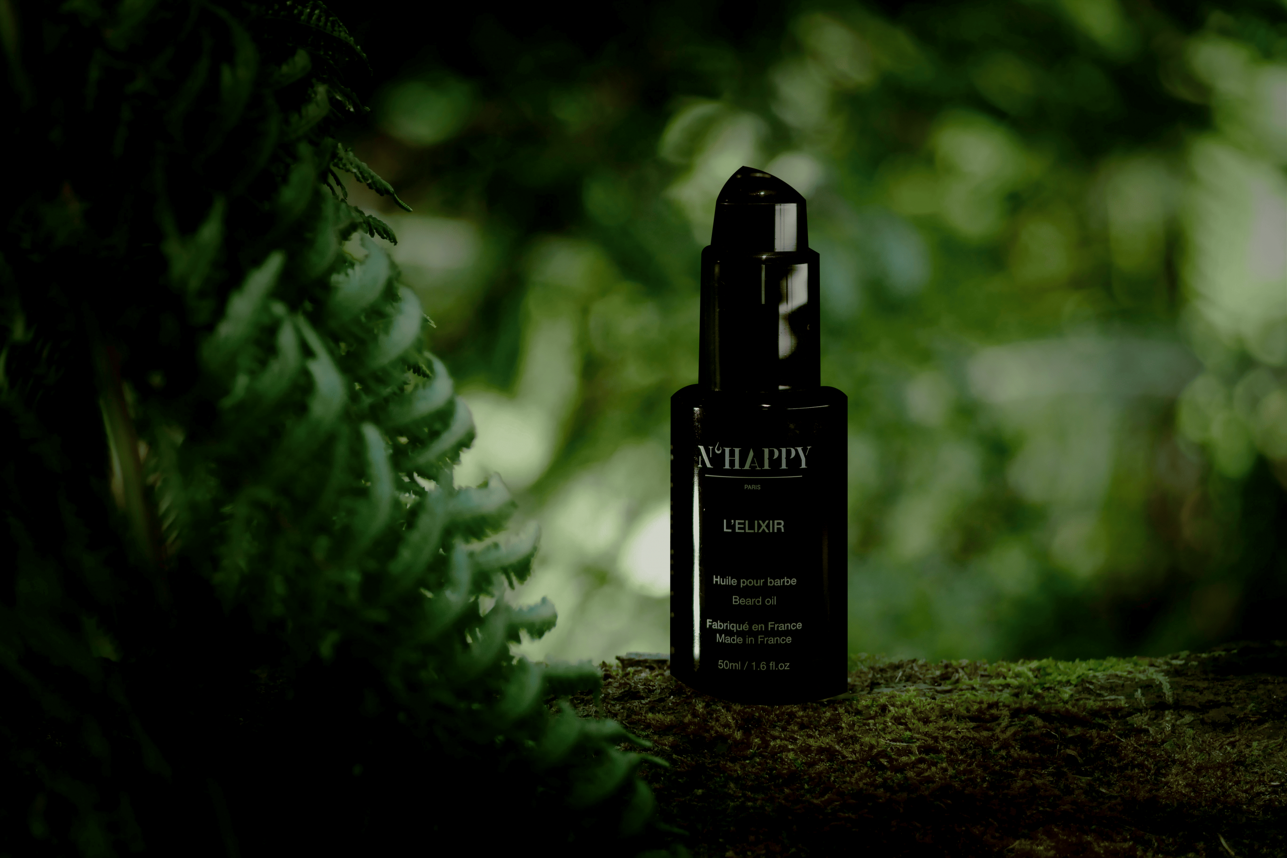 Huile pour barbe Nhappy L’Élixir, flacon noir 50 ml posé sur tronc en forêt, cosmétique bio homme, rendu premium naturel.